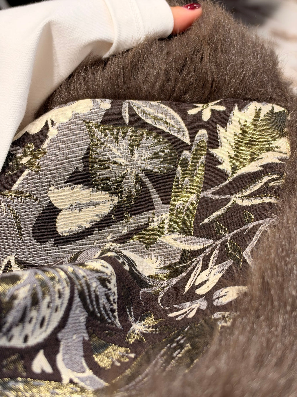 Dettaglio tessuto del gilet: stampa botanica verde e crema su base scura