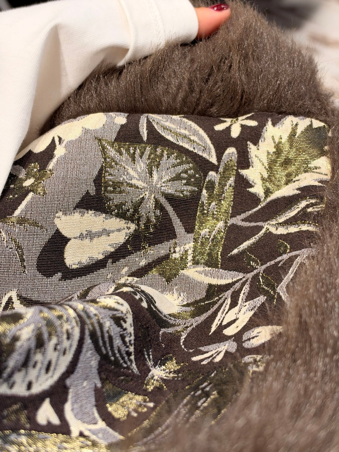 Dettaglio tessuto del gilet: stampa botanica verde e crema su base scura
