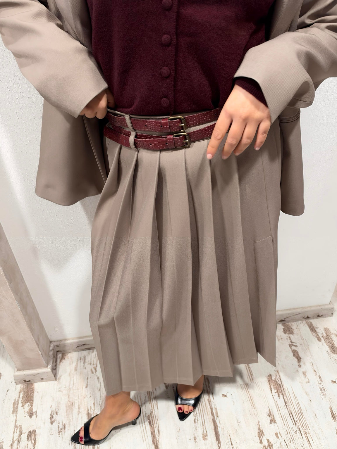 Dettaglio della gonna taupe plissettata e della doppia cintura bordeaux
